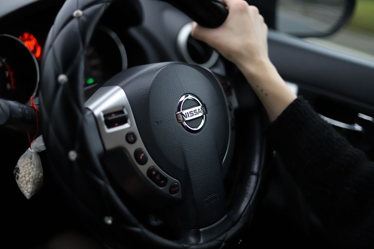 services-01 Close-up shot of a person's hand gripping a Nissan steering wheel. Modern car interior.