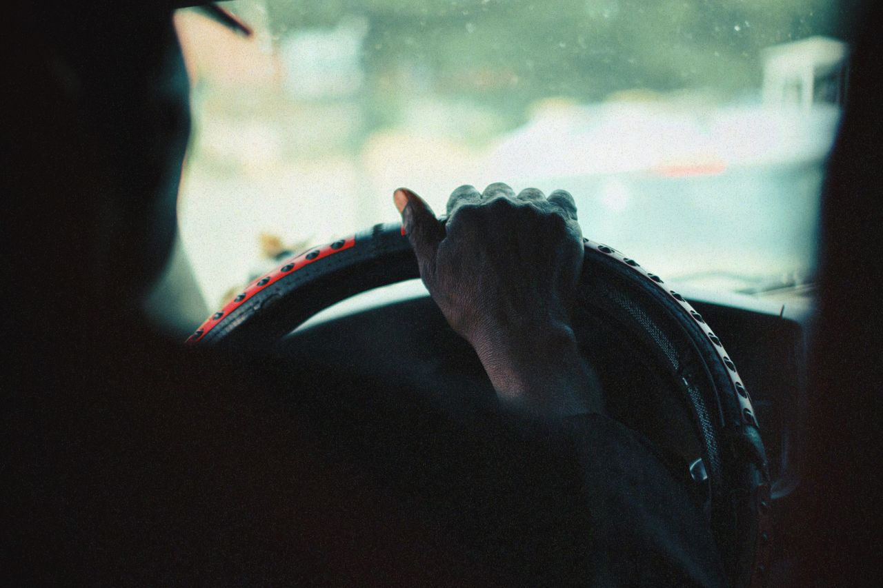 about-02 A close-up view of a person's hand gripping a car steering wheel, captured with a vintage aesthetic.
